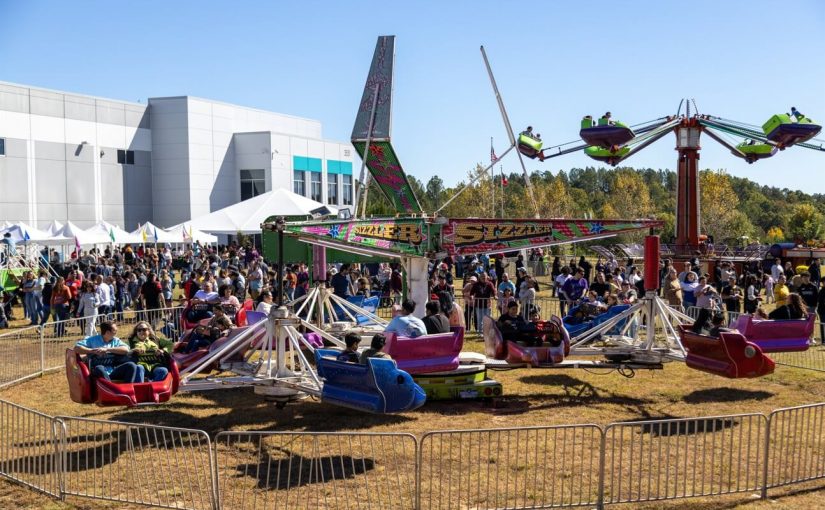 Outdoor carnival event with amusement rides, tents, and a large crowd of guests